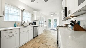 Una cocina moderna con armarios blancos, lavavajillas, estufa y ventilador de techo.