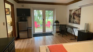 Une chambre avec un lit, un ventilateur de plafond, un bureau et une vue sur une terrasse avec des chaises, accessible par une porte vitrée.