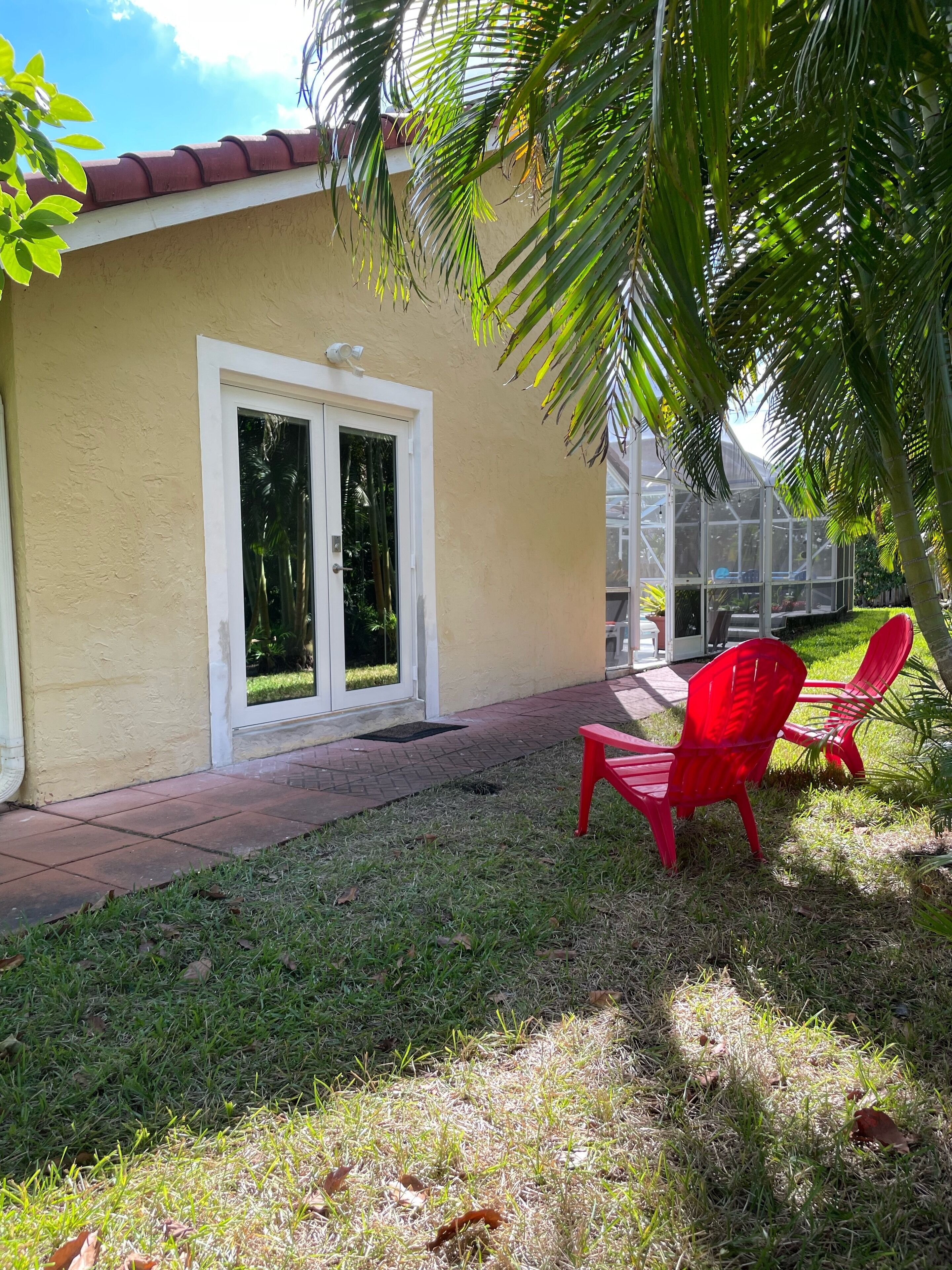 A yellow building with a red roof, a glass door, and a small patio area with red chairs and grass.