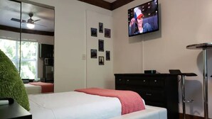 Une chambre à coucher avec un lit, un téléviseur fixé au mur, une commode et un miroir.