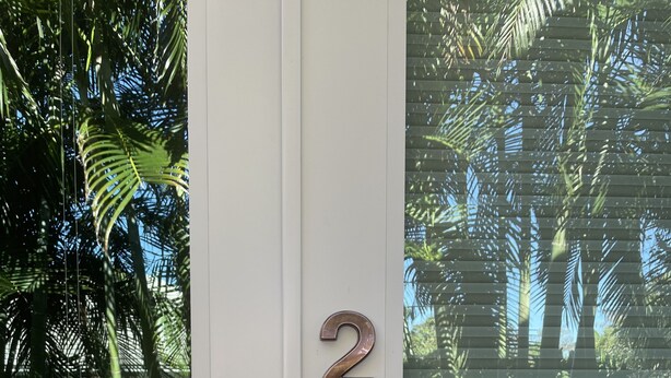 Une porte dotée d’un clavier numérique et d’un trou de serrure, se détachant sur un fond de palmiers et d’un ciel dégagé.