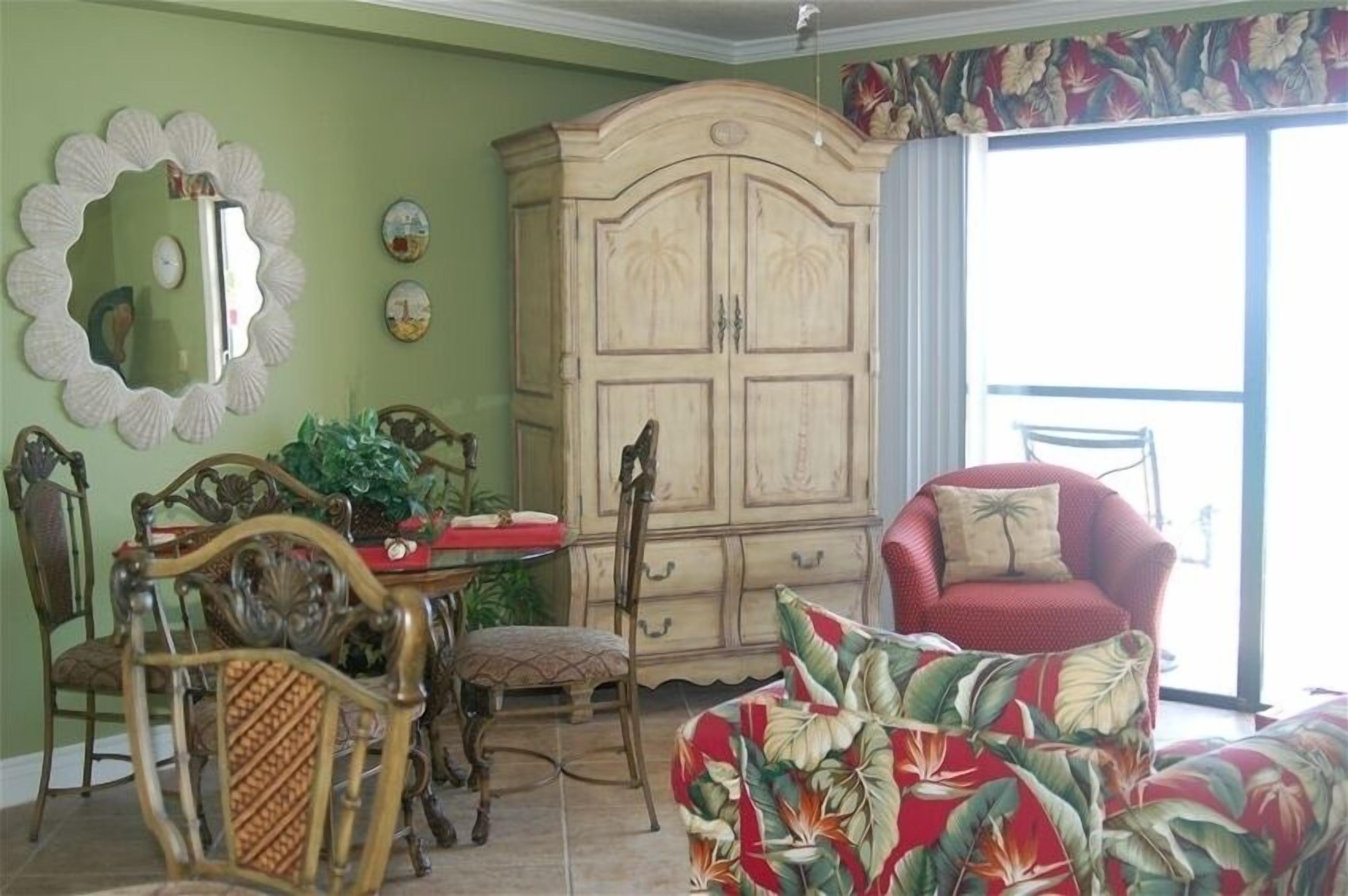 A room with a dining table, chairs, a cabinet, and a red armchair.