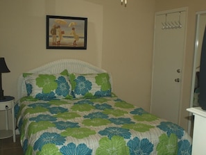 A bedroom with a bed, a nightstand, a door, and a framed picture on the wall.