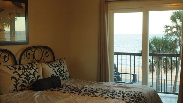 A bedroom with a bed, a balcony with a view of the sea, and a chair.
