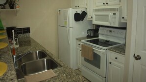 A kitchen with white cabinets, a microwave, an oven, a sink, and a clock on the wall.