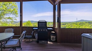 Un patio exterior con una parrilla, asientos y vistas a un paisaje boscoso.