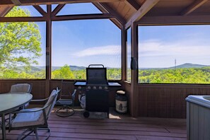 An outdoor patio with a grill, seating, and a view of a forested landscape.