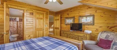 Quarto de cabana de madeira com cama, televisão e uma cadeira.