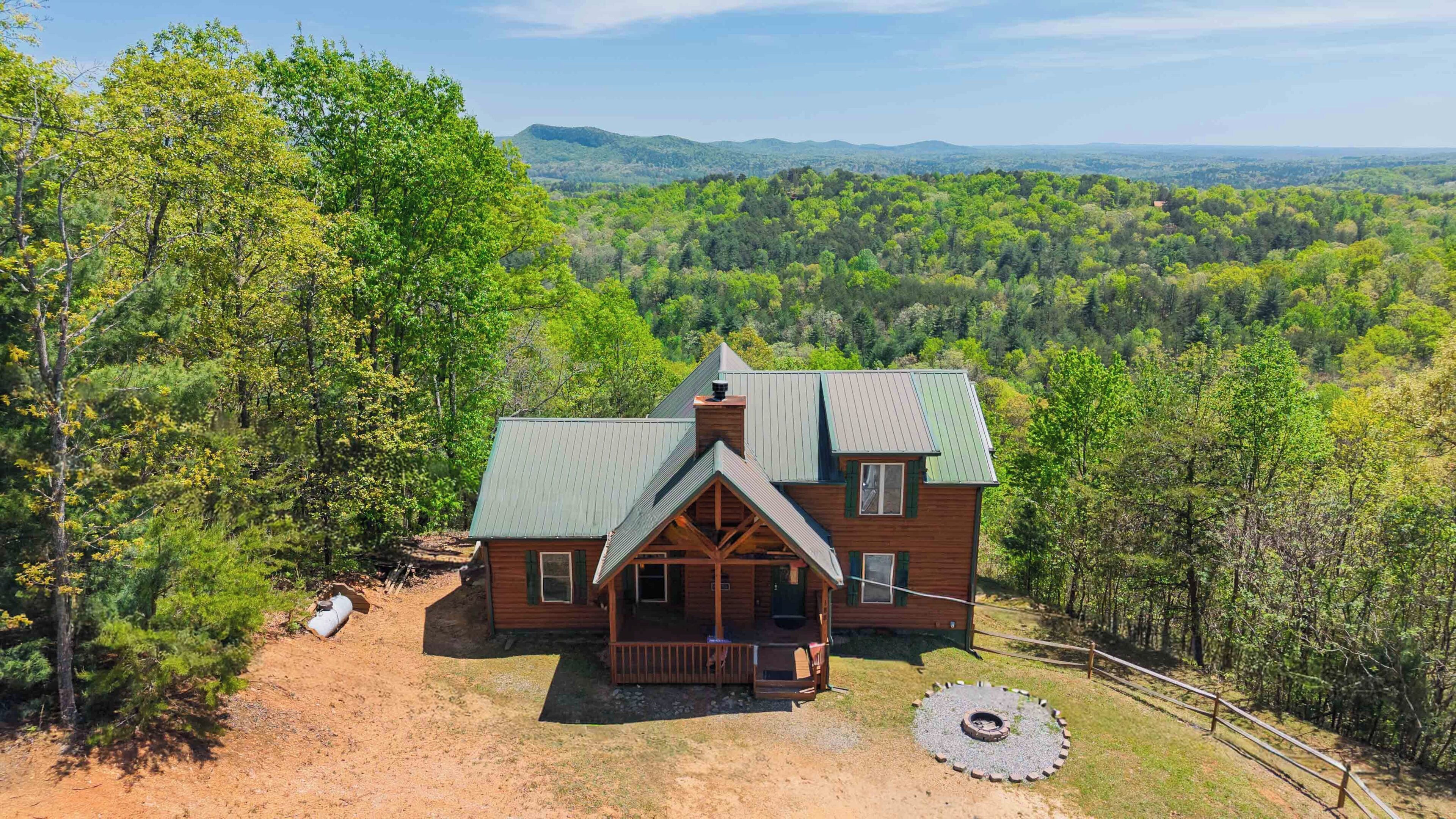 A cabin with a porch, surrounded by forest, with a clear view of the mountains in the distance.