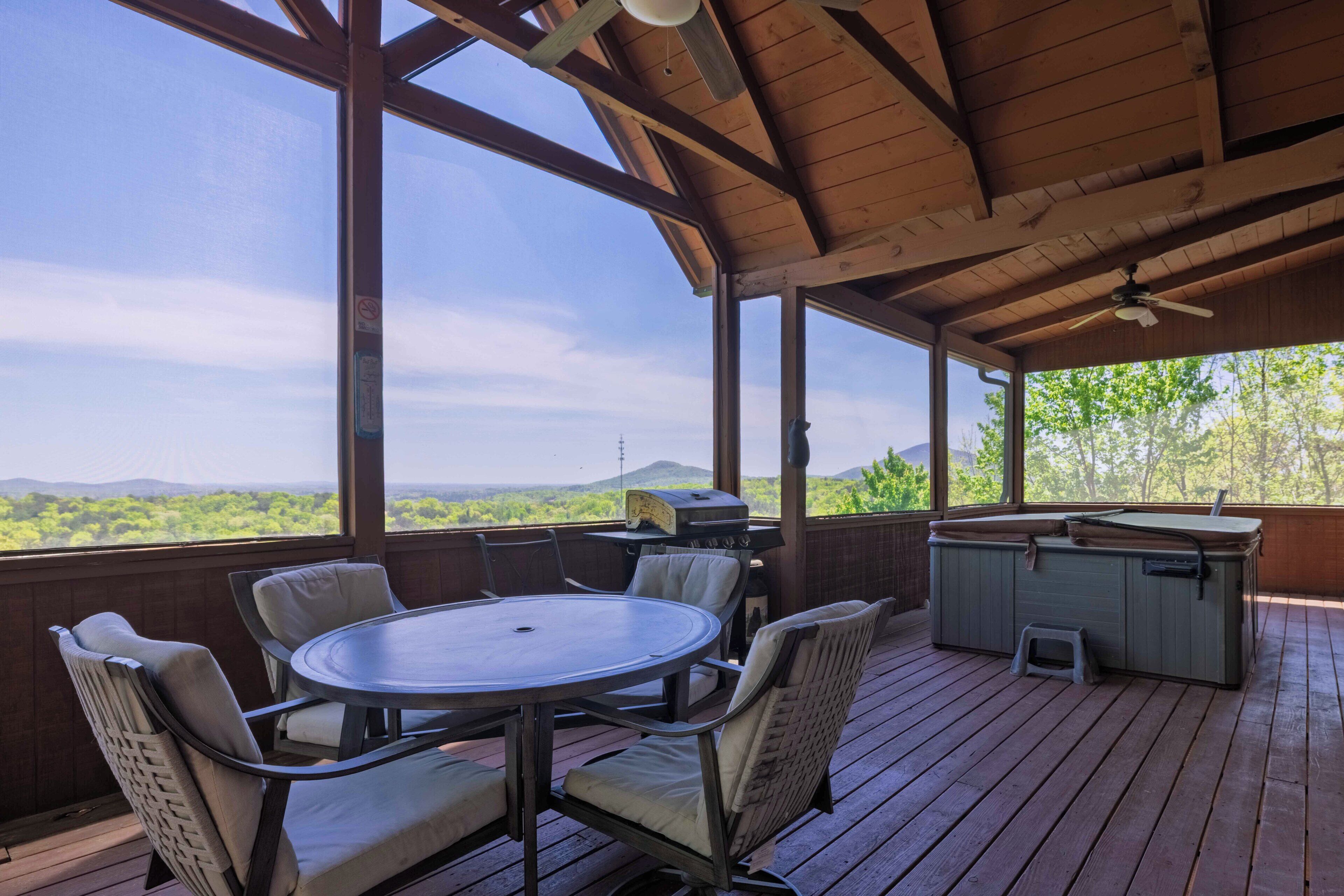 Une terrasse extérieure couverte, avec une table ronde et des chaises, un barbecue et une glacière.