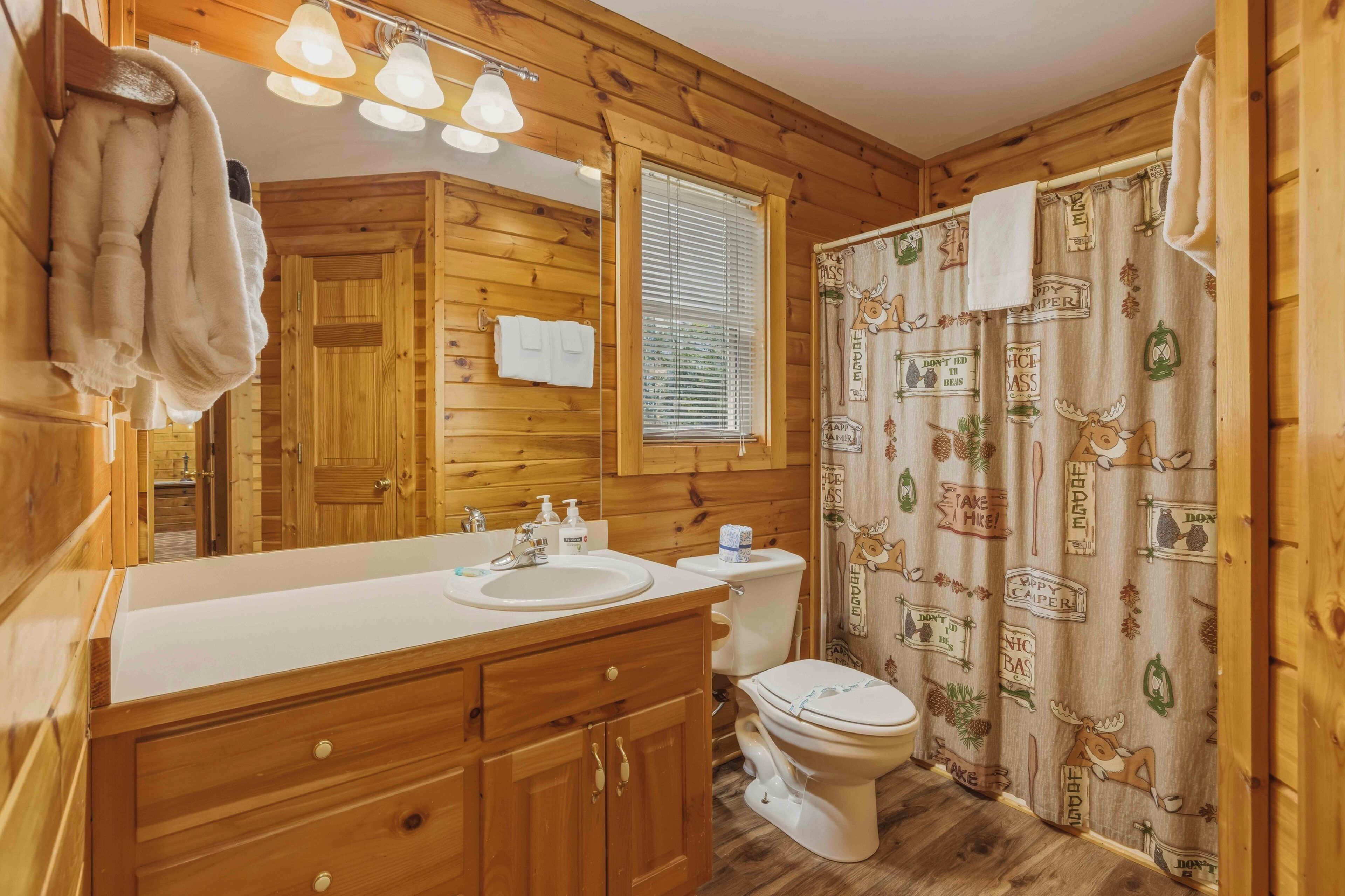 Baño de cabaña de madera con lavamanos, inodoro y cortina de ducha.