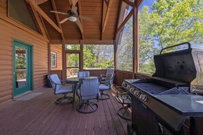 A wooden deck with a grill and seating area, large windows, and a ceiling fan.