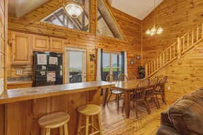 A wooden cabin interior with a kitchen, dining area, and a staircase.