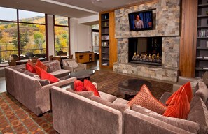 A modern living room with a stone fireplace, comfortable seating, a television, and a view of the outdoors. - Charlie's Slopeside: Ski-In/Out, Ski Valet, Resort Amenities, Pool + Hot Tubs (Avon)