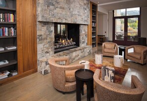 A living room with a stone fireplace, leather armchairs, a coffee table, and bookshelves.