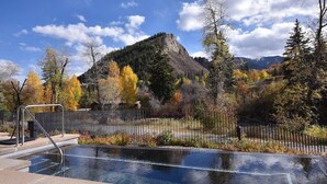 Une piscine extérieure avec vue sur les montagnes, entourée d’arbres et d’une clôture.