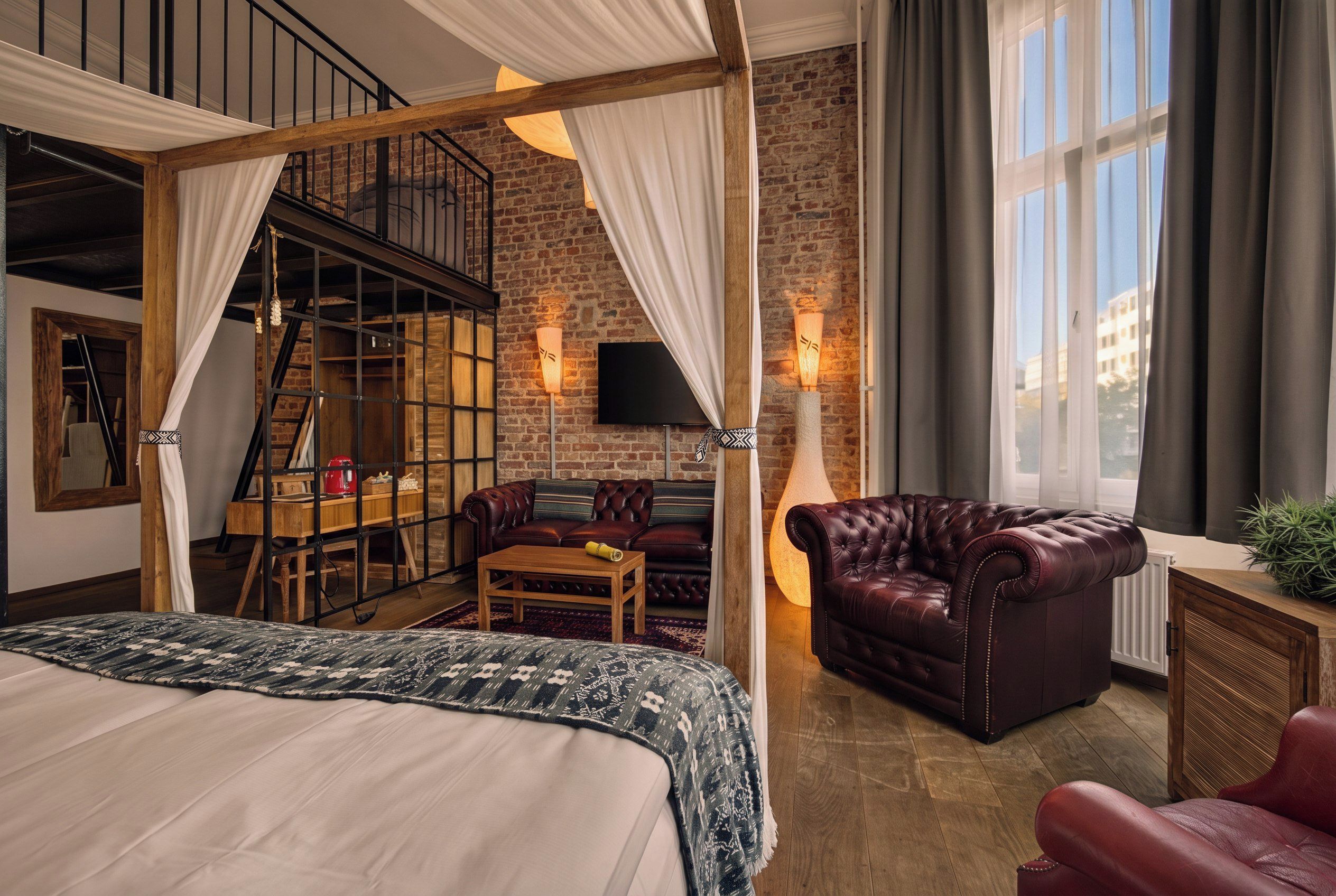 A bedroom with a large bed, a wooden desk, a leather armchair, and a brick wall.