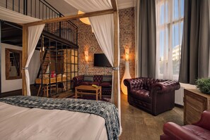 Een slaapkamer met een groot bed, een houten bureau, een leren fauteuil en een bakstenen muur.