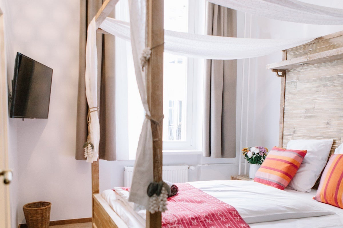 Un lit à baldaquin avec une couvre-lit à motifs rouges, une tête de lit en bois et un luminaire suspendu.