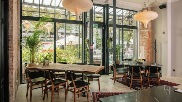 Un restaurante con un gran ventanal, mesas y sillas de madera.