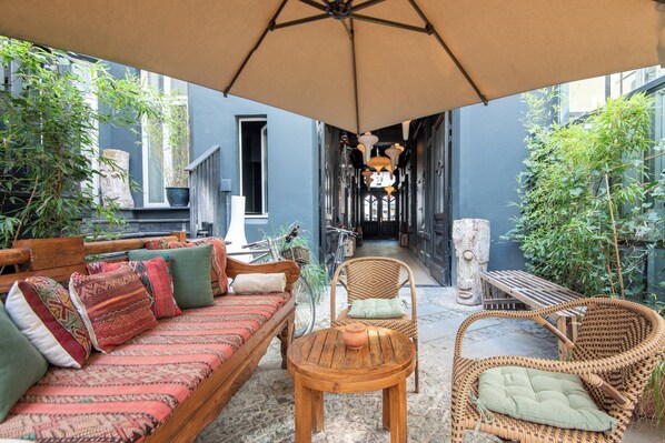 Een gezellig buitenverblijf met een bank, stoelen en een tafel, beschut onder een grote parasol.