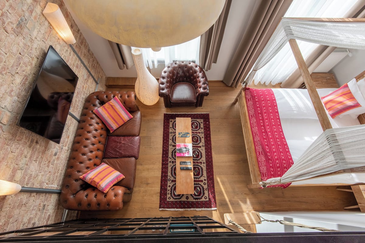 Une pièce de style loft avec un lit en mezzanine, un canapé en cuir, un tapis à motifs et un grand luminaire suspendu.