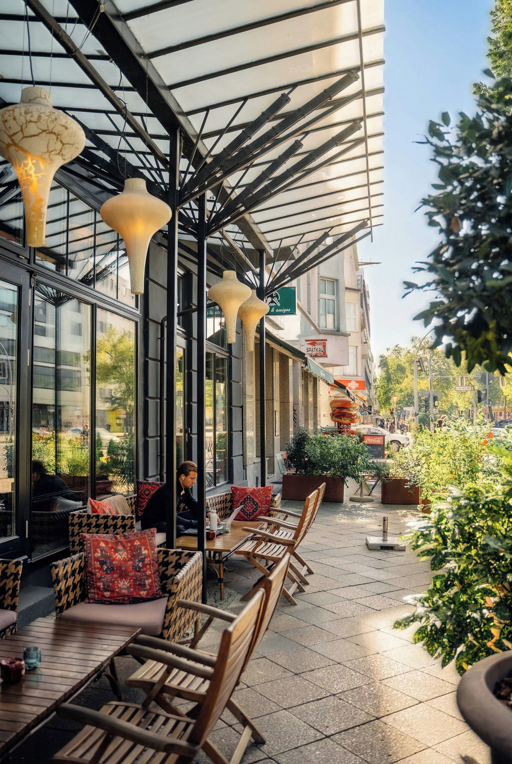 Un espace extérieur aménagé avec des tables et des chaises, une allée couverte et des plantes en pot.
