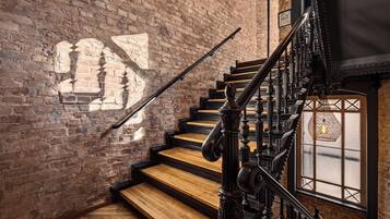 A staircase with wooden steps and black balusters, leading to a landing with a wrought iron railing.