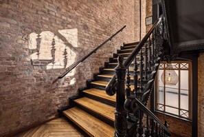 A staircase with wooden steps and black balusters, leading to a landing with a wrought iron railing. - Lulu Guldsmeden Hotel  (Berlin)