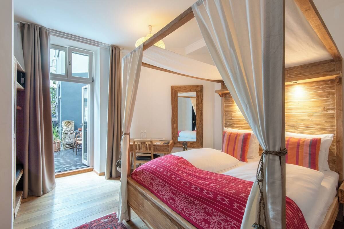 Un lit à baldaquin avec une couvre-lit rouge à motifs, une tête de lit en bois et un grand miroir au-dessus.