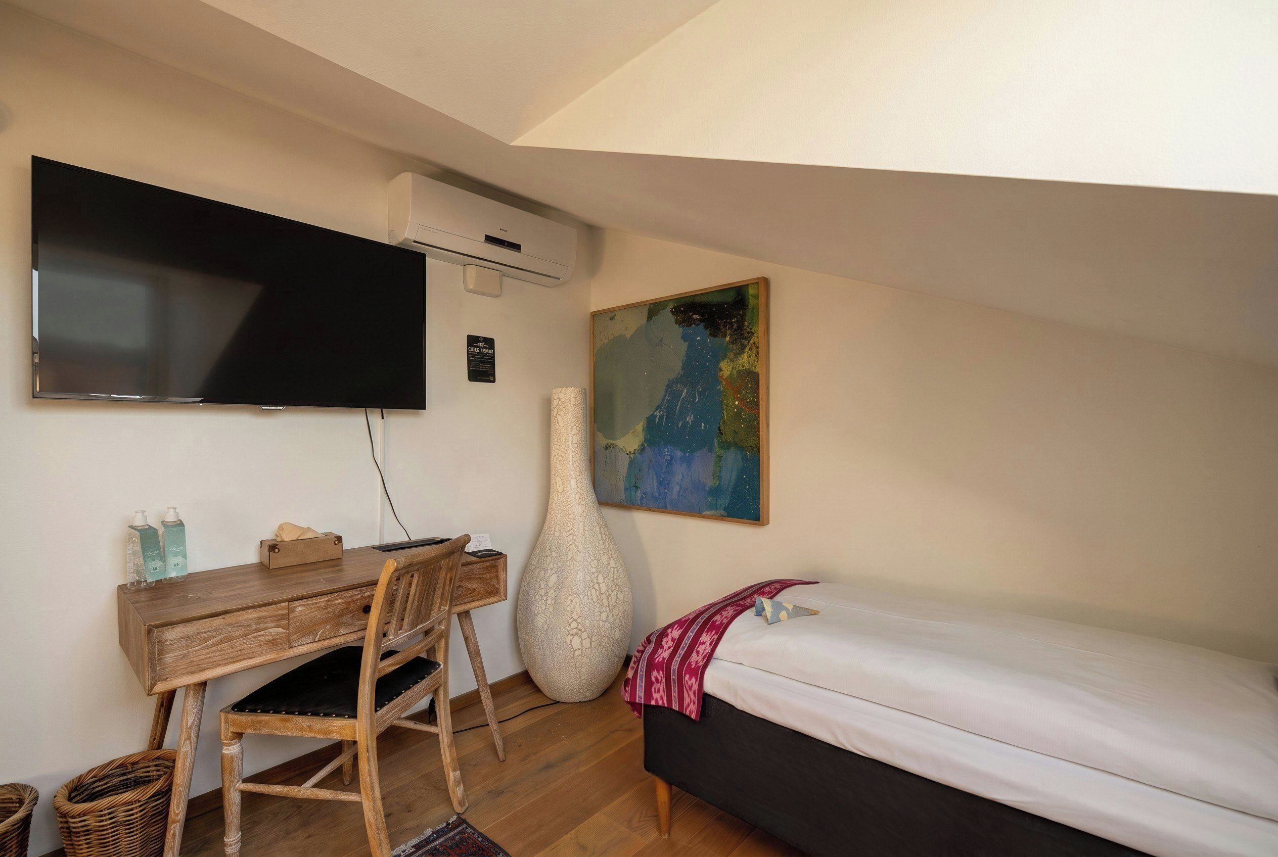 Quarto com cama, escrivaninha, cadeira, televisão e um quadro.