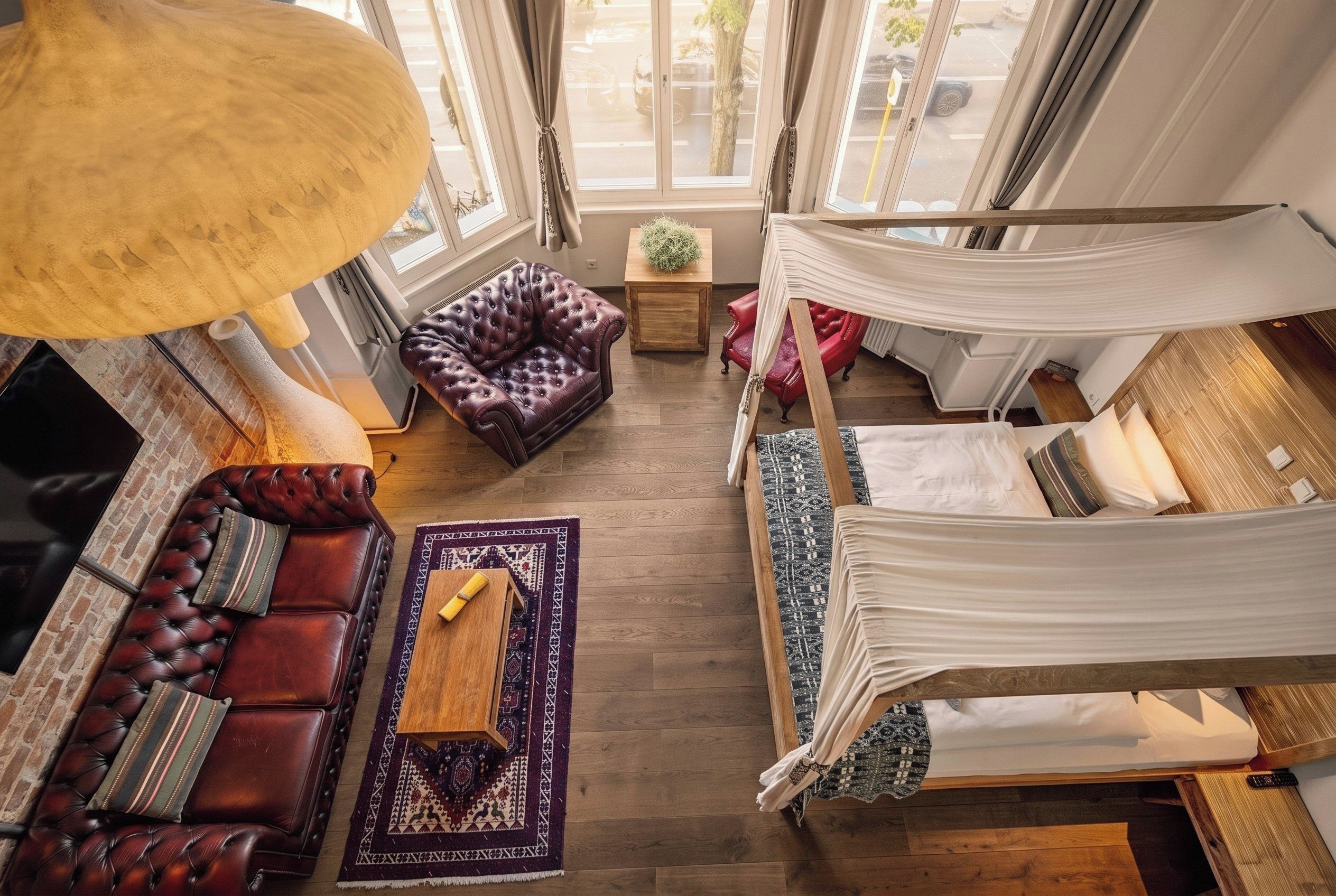 Een ruime kamer met een leren bank, een rode fauteuil, een bed met hemelbed en een groot raam met uitzicht op de straat.