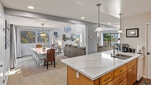 Una cocina moderna con una isla grande, una zona de comedor con mesa y sillas, y una sala de estar con sofá y mesa de centro.