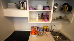 A kitchen with a black induction cooktop, a stainless steel sink, and shelves above holding dishes, cups, and kitchen utensils. - Splendid Star..... San Mark's Square all inclusive WiFi (Venezia)