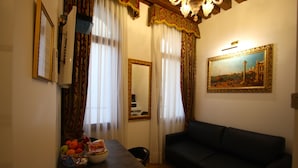 A living room with a dark sofa, a dining table with fruit, a mirror, and a painting on the wall. - Splendid Star..... San Mark's Square all inclusive WiFi (Venezia)