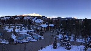 Ein Resort mit einem zentralen Poolbereich, umgeben von Gebäuden mit schneebedeckten Dächern, und einem Berg im Hintergrund.
