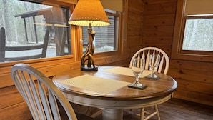 A wooden dining table with two chairs, a lamp, and a view of a snowy outdoor area.