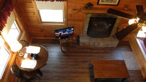 A cozy cabin interior with a wooden floor, a fireplace, a dining area with a table and chairs, and a sofa.