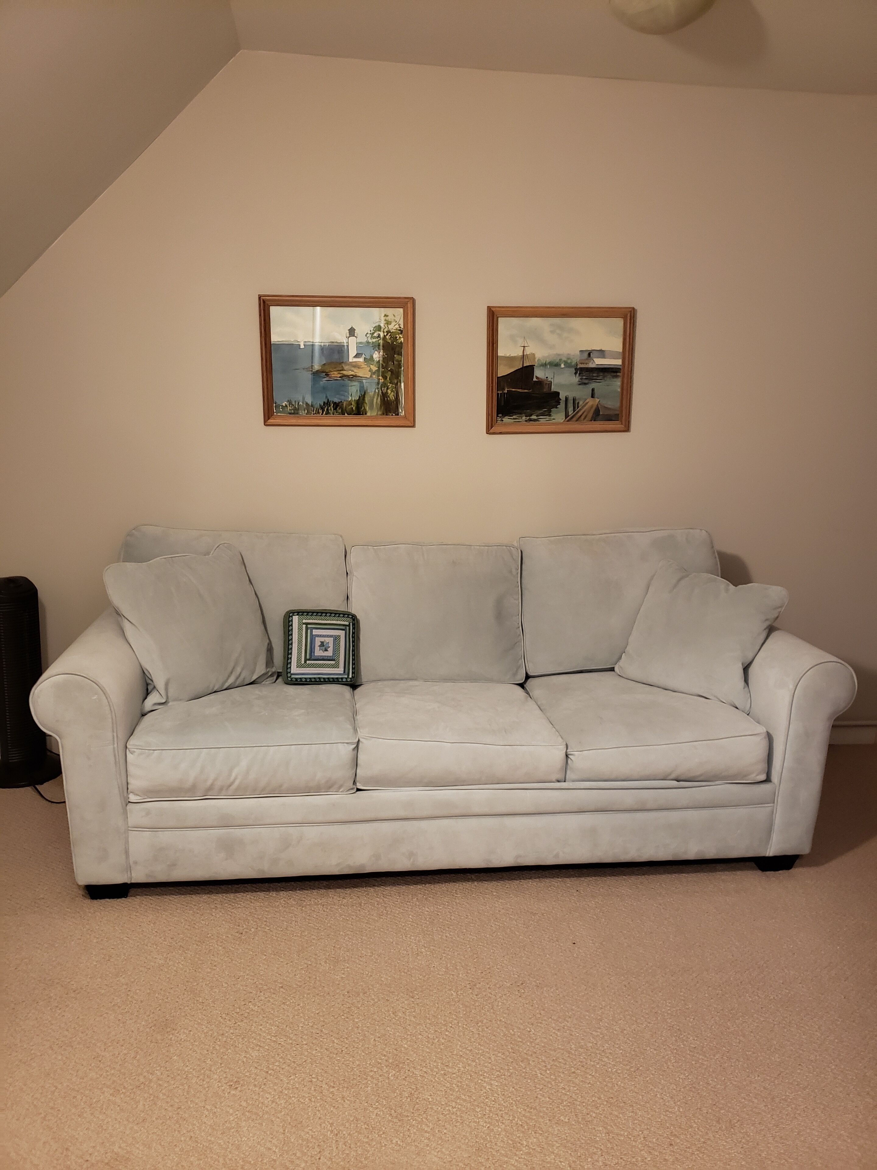 Un canapé de couleur claire, agrémenté d’un coussin décoratif et surmonté de deux tableaux encadrés accrochés au mur.