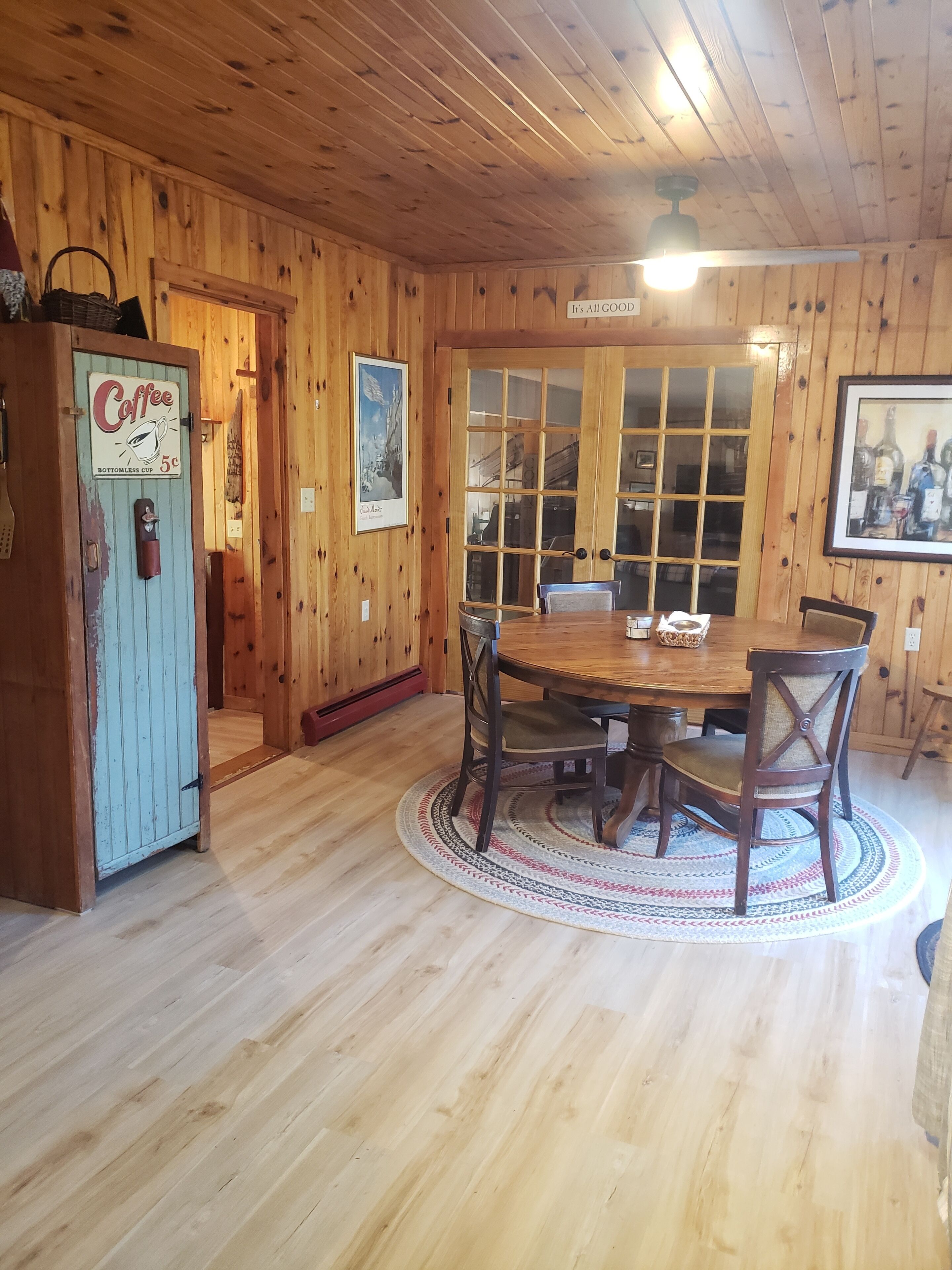 Interior de fusta amb taula de dinar, cadires, una cafetera i una porta amb un panell de vidre.
