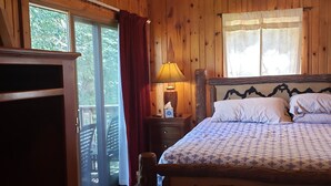 Ein Schlafzimmer einer Holzhütte mit einem Bett, einem Nachttisch, einer Lampe, einem Deckenventilator und einem Fenster mit Vorhängen.