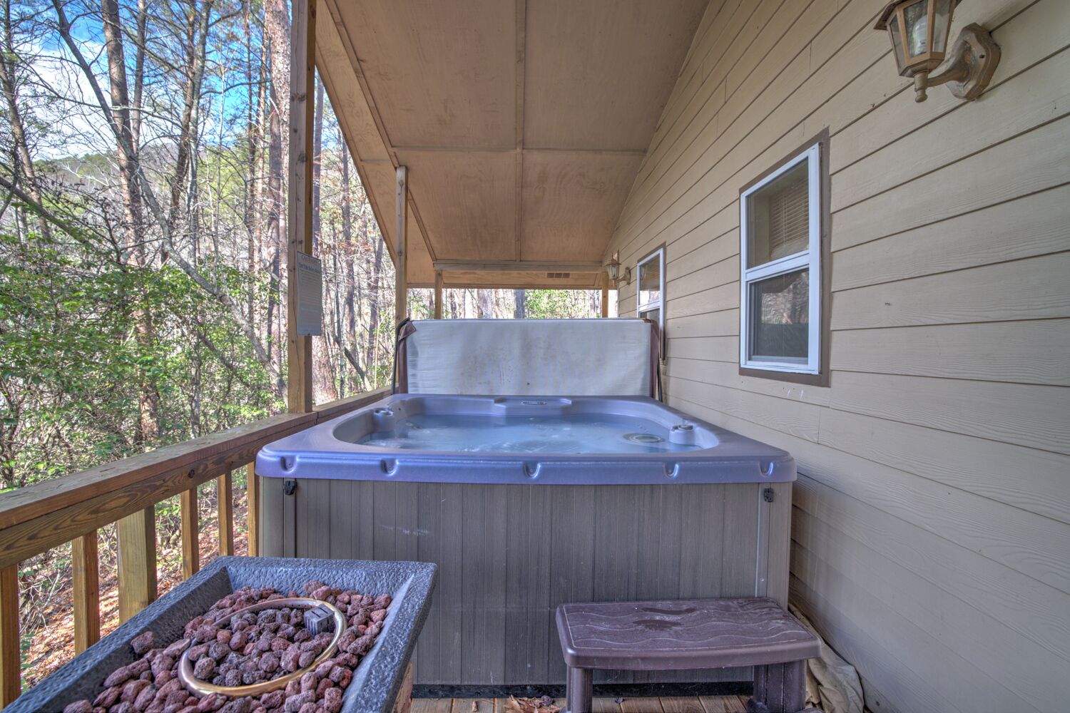 Un bain à remous sur une terrasse en bois, avec une rambarde en bois et un petit banc.