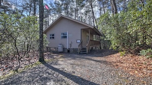 A cabin with a gravel driveway, surrounded by trees.