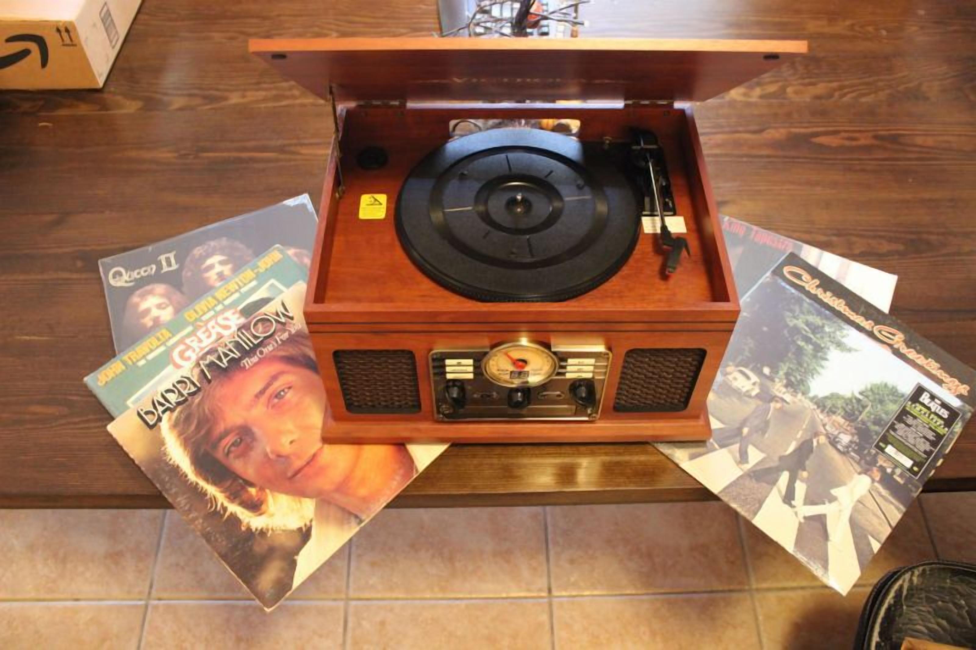 A wooden record player with vinyl records placed on the floor beside it.