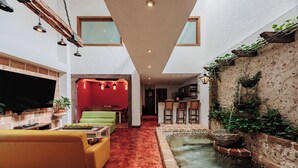 Een ruime woonkamer met een rood tapijt, een groene bank, een televisie en een klein fonteintje.