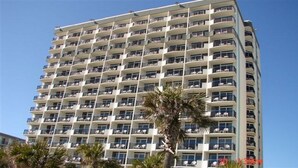 A high-rise hotel with multiple balconies, a clear sky, and palm trees in the foreground. - "Direct" Ocean Front 9th Floor cozy coastal cottage Reasonable Rates (Myrtle Beach)