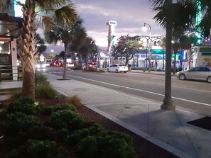 A street view with palm trees, a sidewalk, and a road with cars. - "Direct" Ocean Front 9th Floor cozy coastal cottage Reasonable Rates (Myrtle Beach)