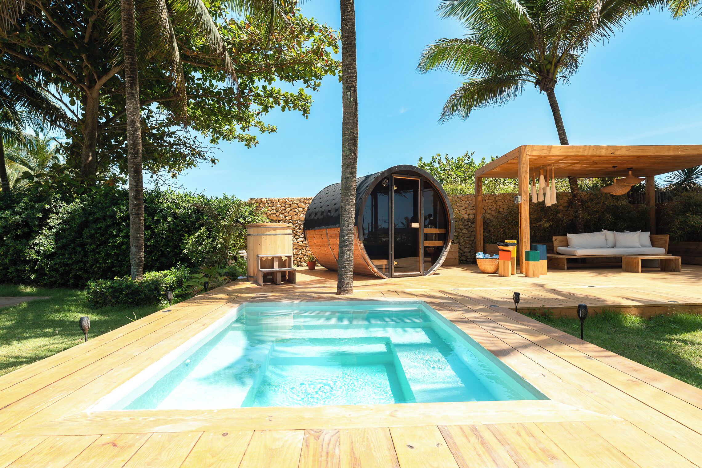 Um deck de madeira com piscina, uma pérgula de madeira e uma estrutura esférica com porta de vidro.
