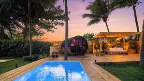 Eine Holzterrasse mit Schwimmbecken, einer kugelförmigen Struktur mit Glaswänden und einer Sitzgelegenheit mit einer Lampe.