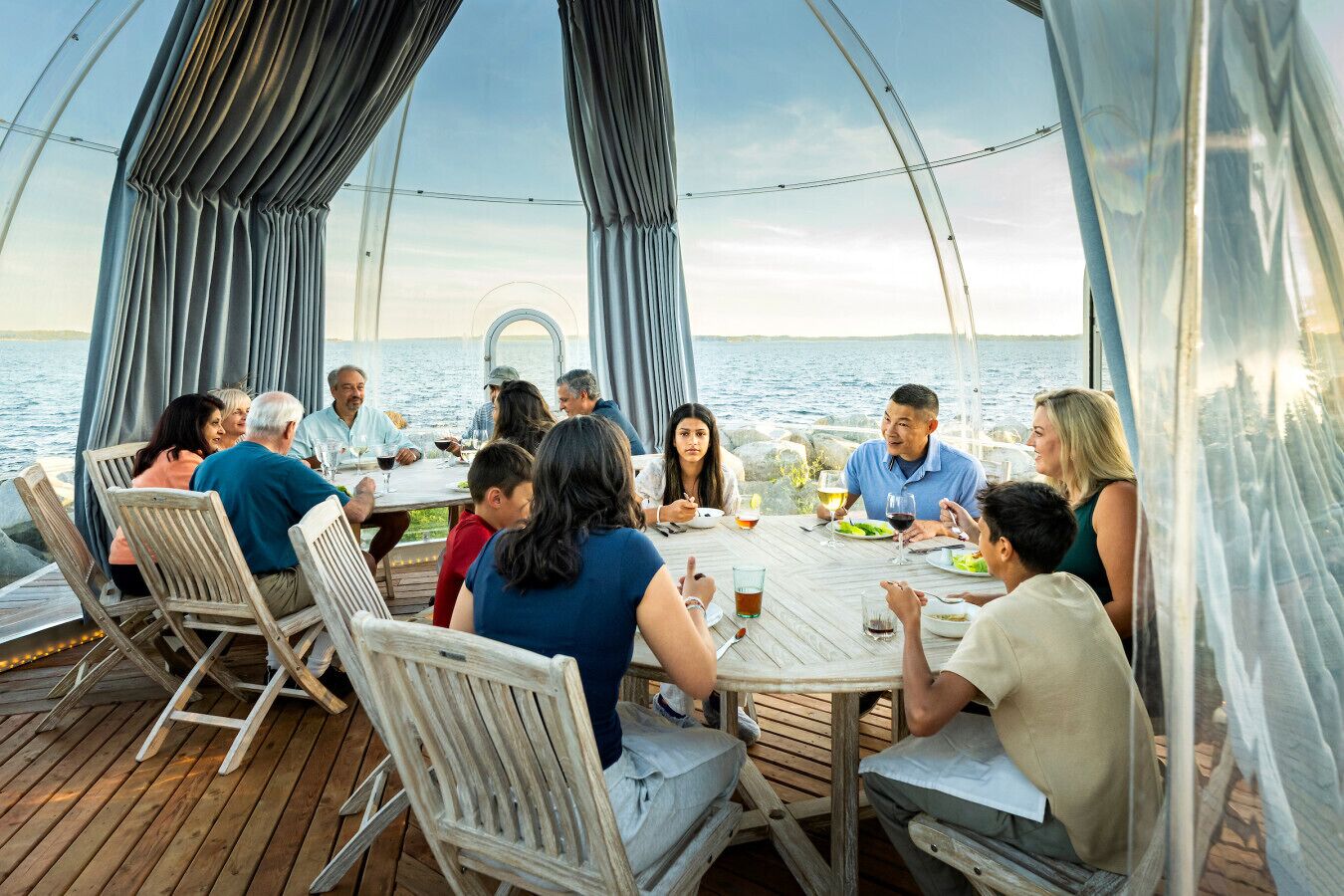 A group of people dining on a wooden deck with a view of the water.